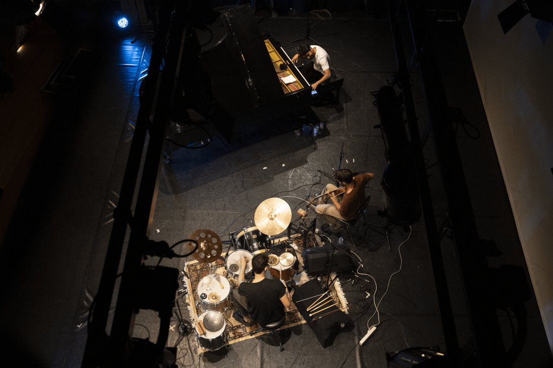 Fotografia de cena a cores, vista de cima, mostrando dois músicos a tocar instrumentos de percussão e de cordas.