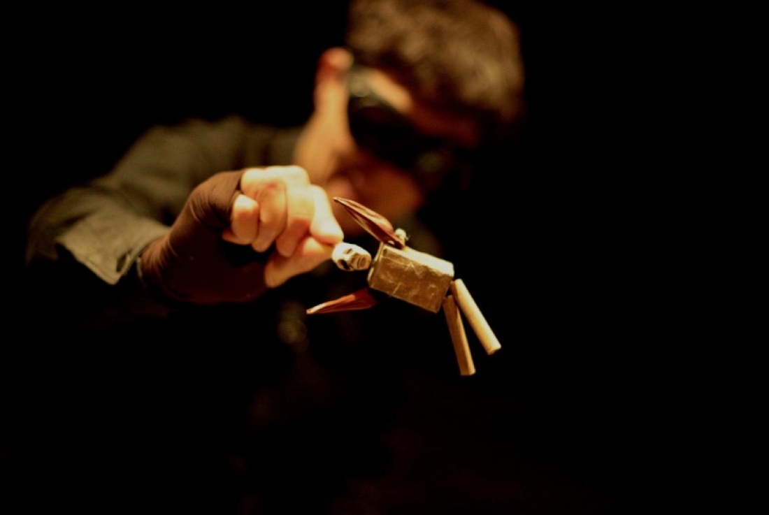 A puppeteer manipulates a small jointed puppet under a spotlight
