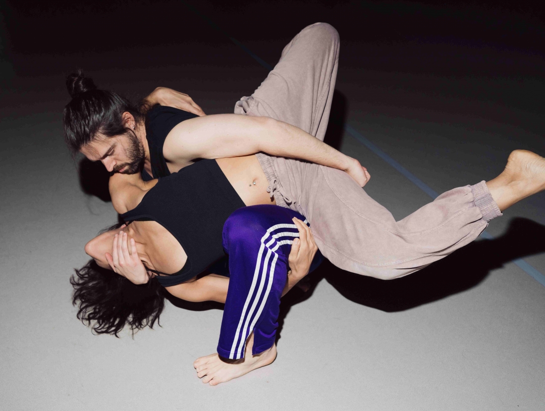 Two people are holding each other, their bodies entwined on a grey floor.
