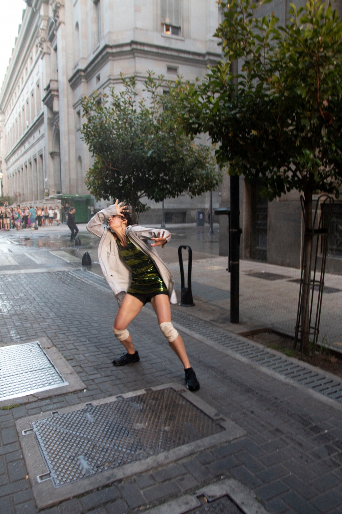 Uma rua estreita e escura, pessoas fotografam uma pessoa agachada no chão. Atrás dela, há fumo.