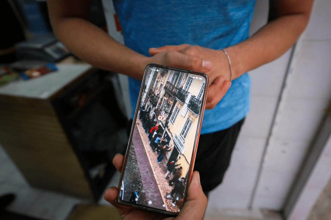 Fotografia a cores. Em grande plano, um telemóvel que mostra no ecrã as imagens da operação policial na Rua do Benformoso, em Lisboa.