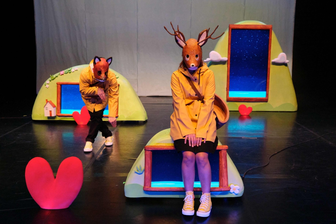 On stage, two performers wearing animal masks and yellow raincoats.