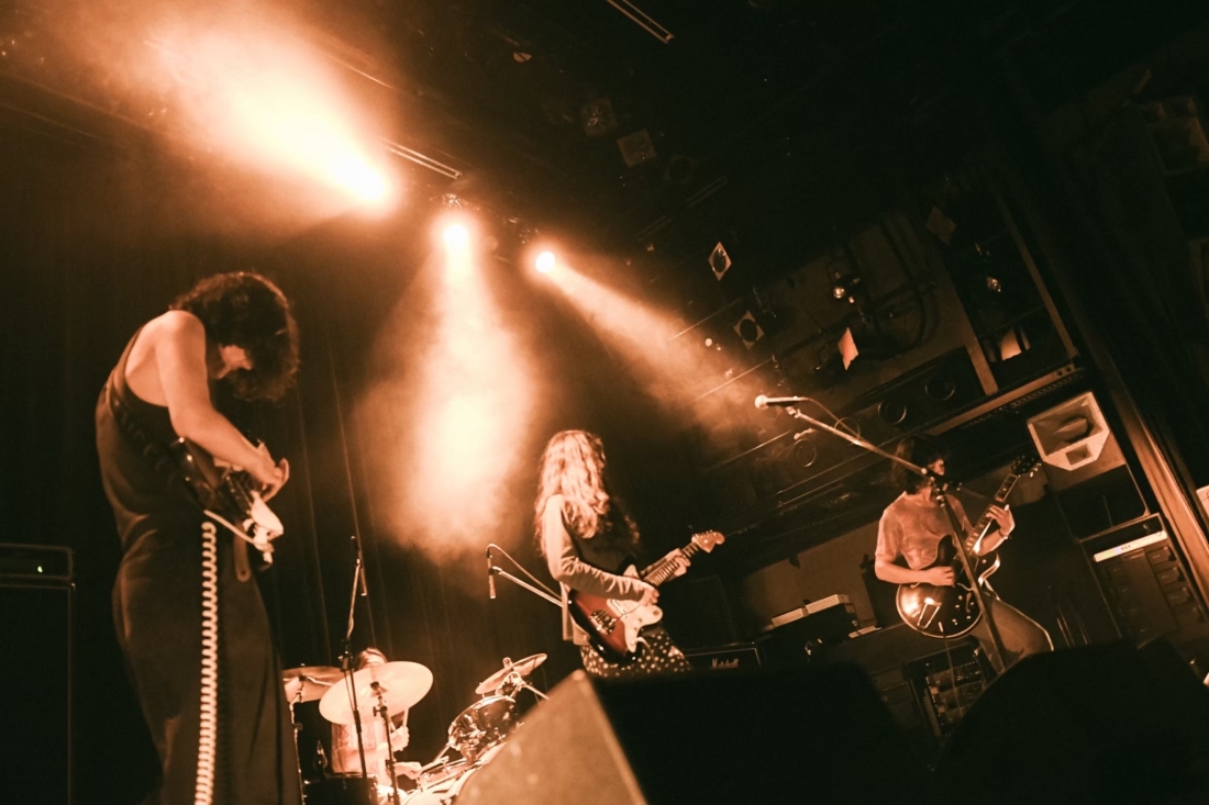 Four musicians are performing on stage during a concert, illuminated by amber spotlights.