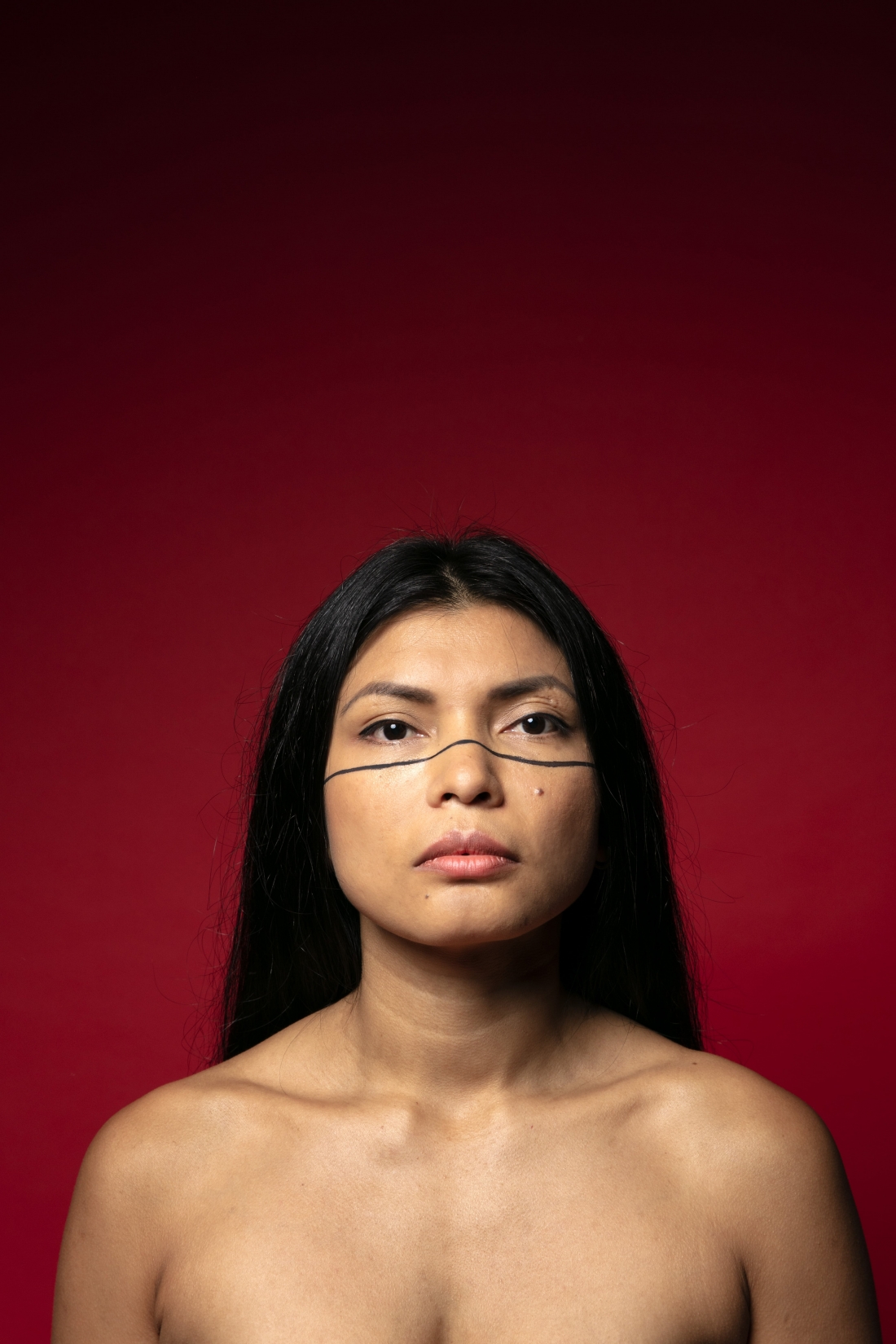 Retrato a cores de Zahy Tentehar. Diante de um fundo vermelho-escuro, o seu rosto encara-nos com confiança. Tem cabelo liso, olhos pretos e uma linha preta pintada por baixo dos olhos que atravessa o rosto.