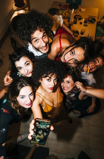 Fotografia a cores. Um grupo de amigos tira uma selfie durante um jantar em casa. 