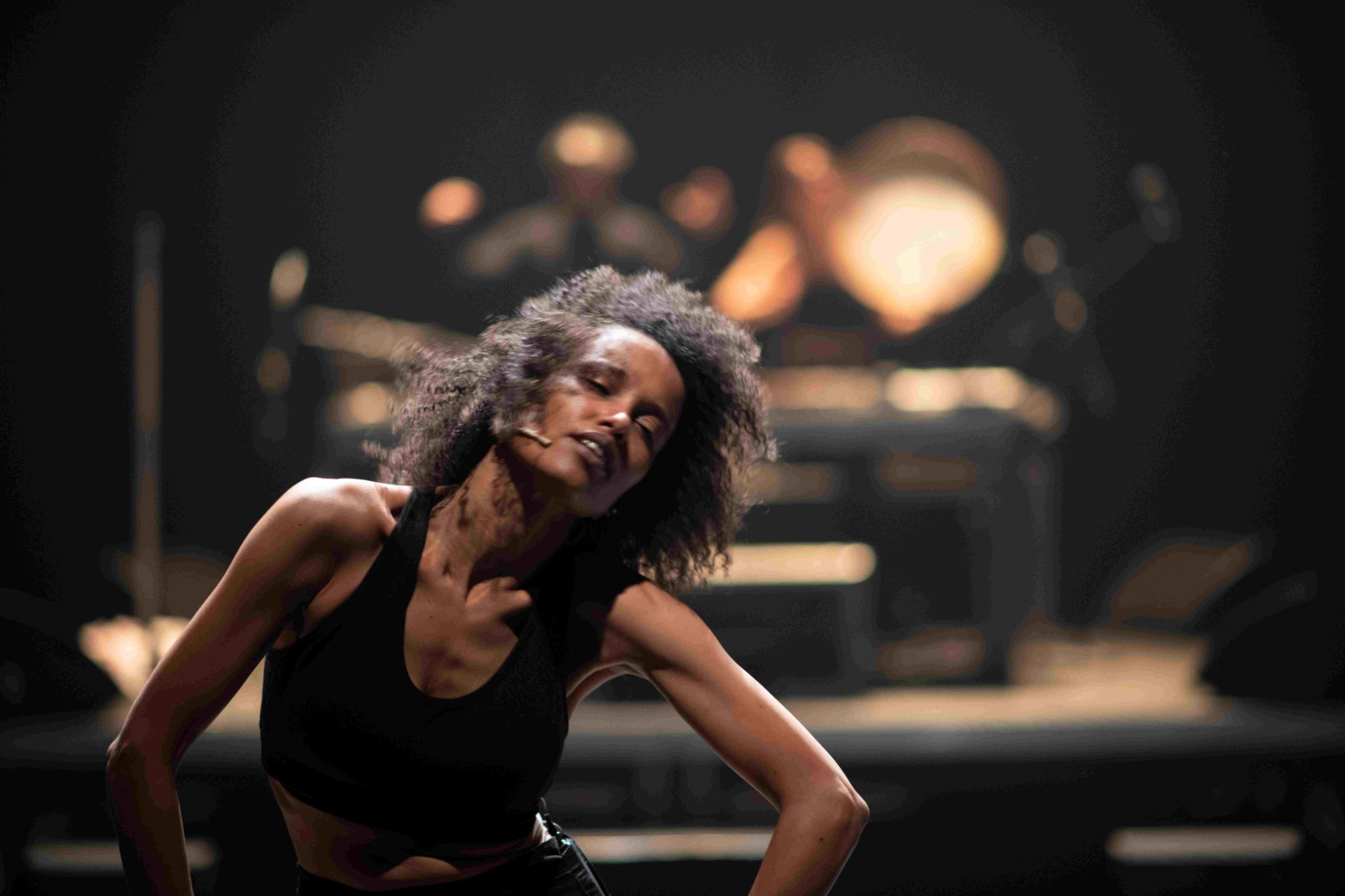 A performer tilts her head whilst bending her body slightly, with musicians blurred in the background.