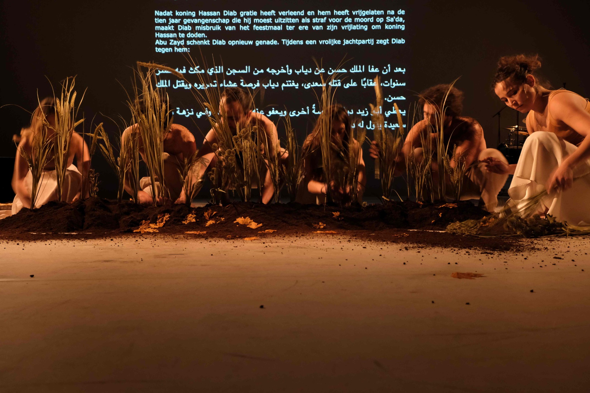 Performers kneel as they plant vegetation in a patch of earth on the stage.