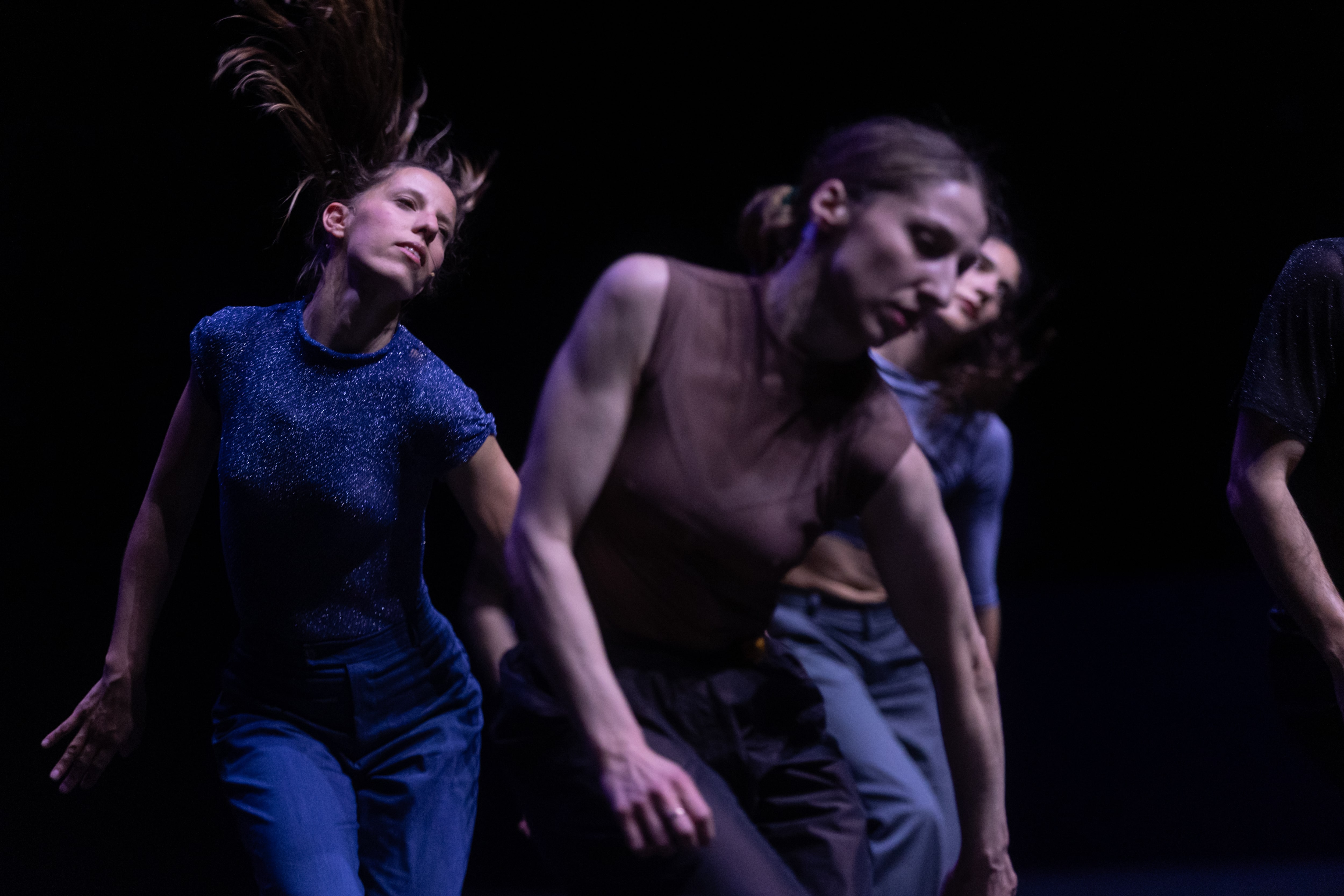 olor stage photograph of a performer moving her torso and head in the opposite direction of her hips, while other performers in the background mirror the same movement.