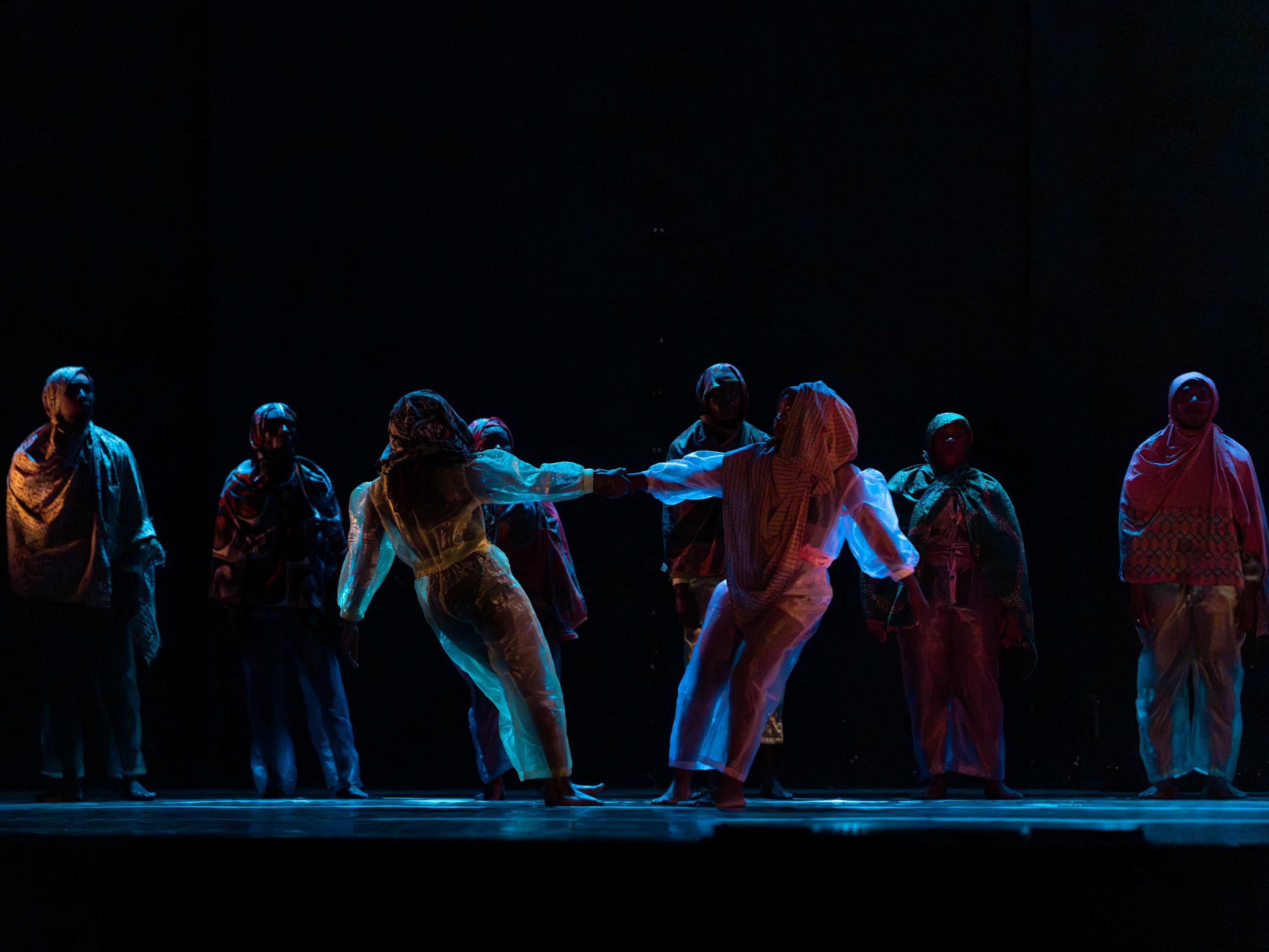Two dancers are balancing, holding hands, in the centre of the stage, bathed in blue light.