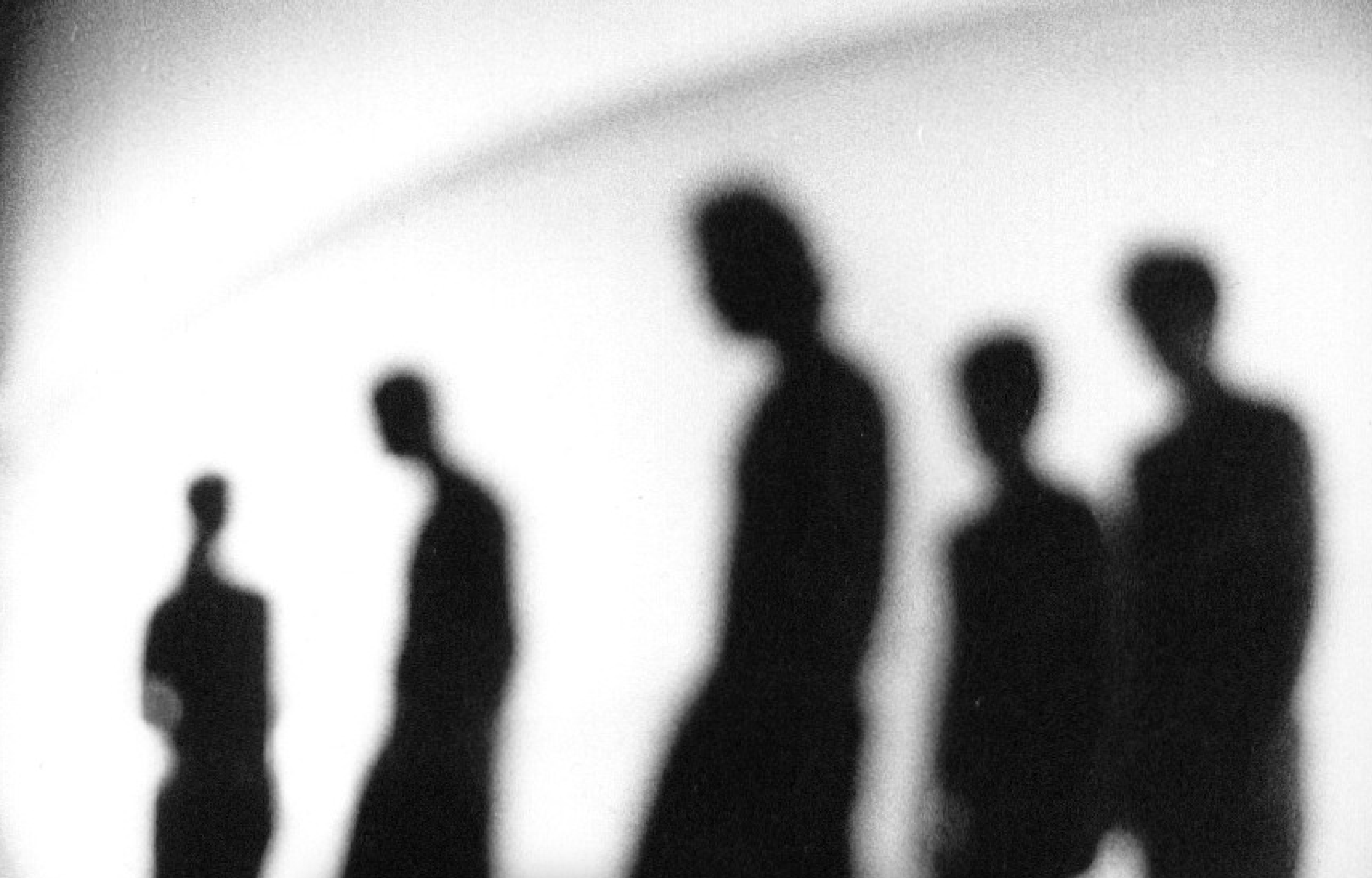A blurred black-and-white image showing five human silhouettes scattered across the space.