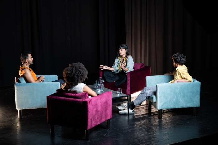 Fotografia a cores. No centro do palco do Pequeno Auditório do Teatro Rivoli, numa espécie de círculo, Ellen Lima Wassu, Gessica Correia Borges, Luca Argel e ROD conversam.